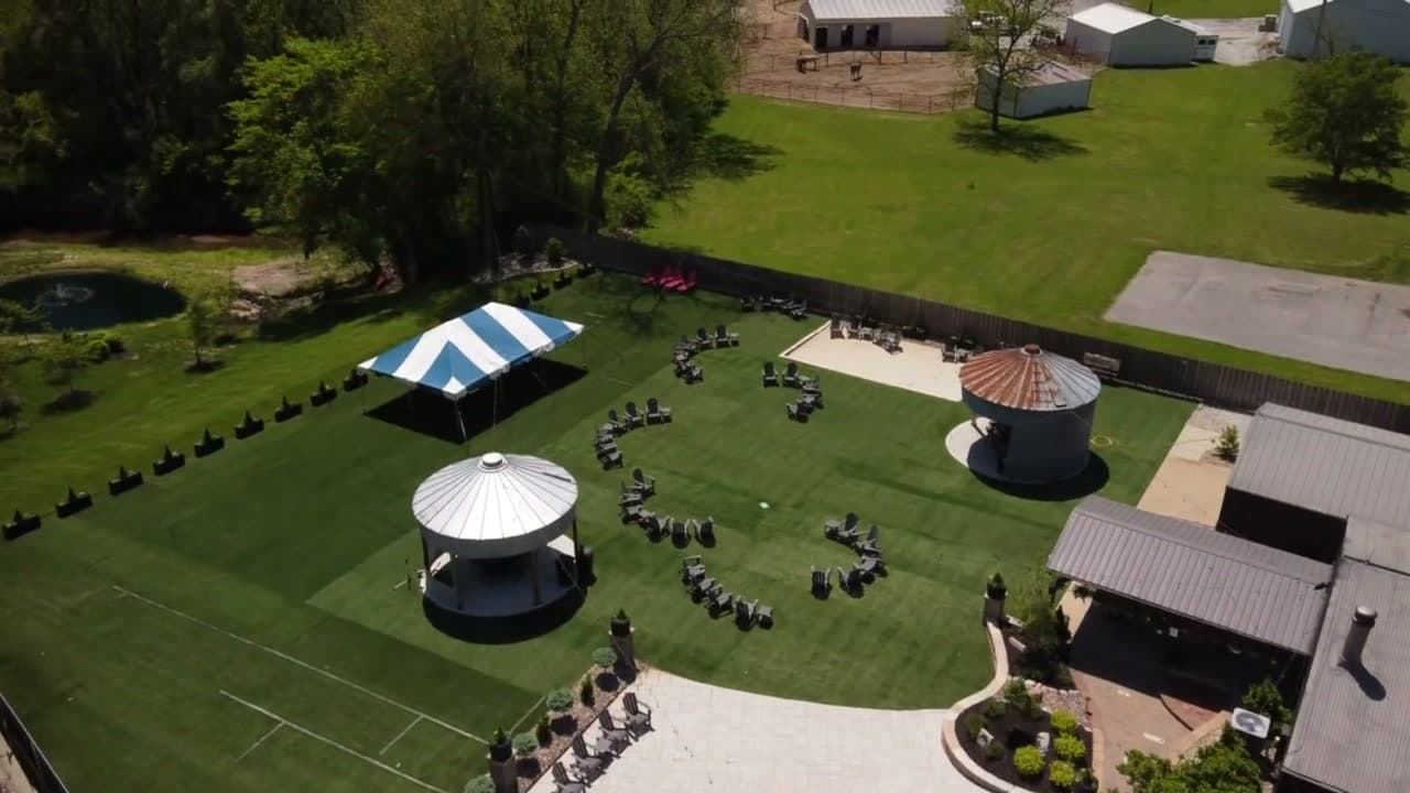 Aerial view of full venue grounds with tent, gazebos, and tree line